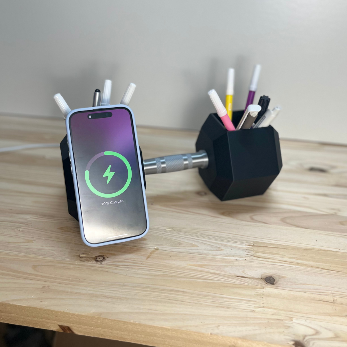 Das Smartphone liegt der Hantel auf und wird durch die Magnete des MagSafes sicher gehalten und dabei aufgeladen. Hier wird die Funktionalität des Ladestation im Hantellook gezeigt. Zusätzlich können die Hohlräume der Hantel als Stifteablage genutzt werden.